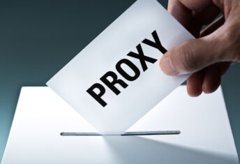 Voter's hand holding a proxy vote ballot, inserting the vote card into the ballot box.