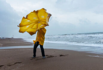Person on a beach trying to hold an umbrella on a windy day